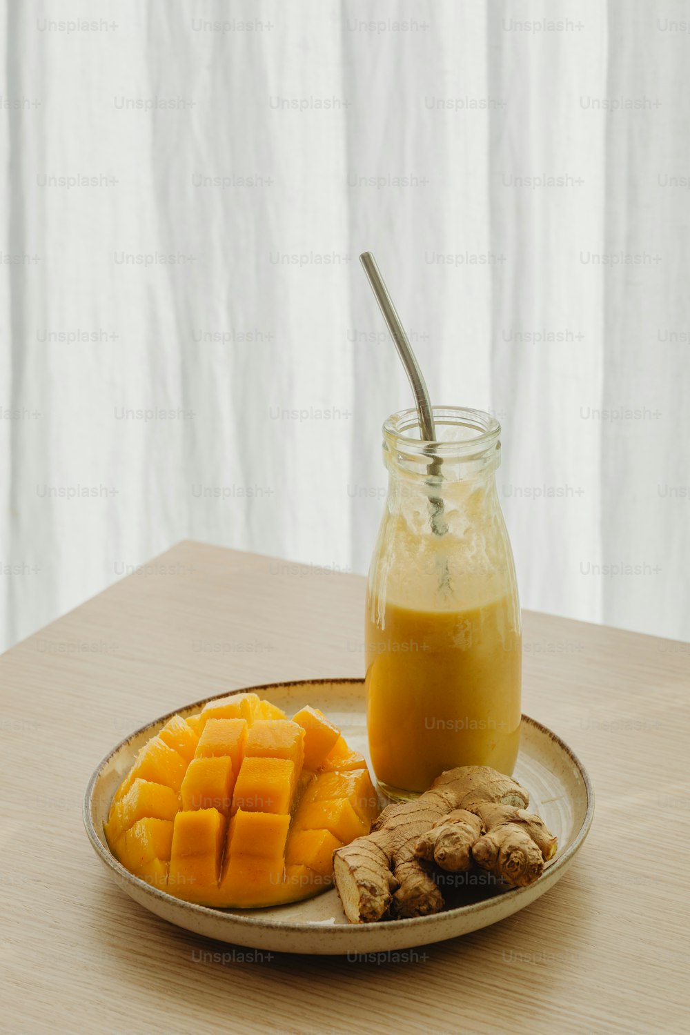 a glass of orange juice next to sliced mangoes and ginger on a plate
