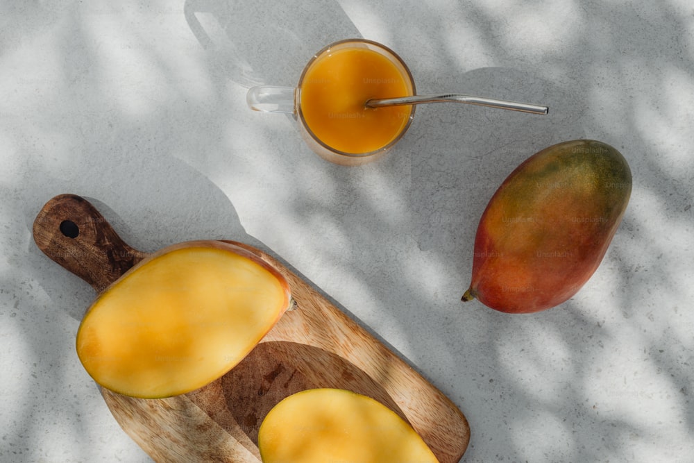 una tabla de cortar de madera cubierta con rodajas de mango junto a un vaso de jugo de naranja