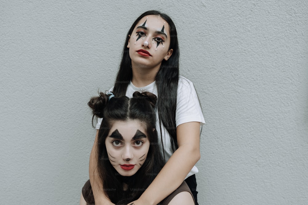 Zwei Mädchen mit Make-up im Gesicht, die nebeneinander sitzen