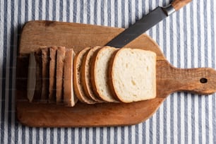 una barra de pan en rodajas en una tabla de cortar con un cuchillo