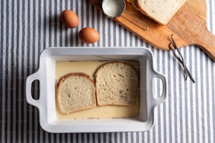 a loaf of bread in a white dish next to eggs