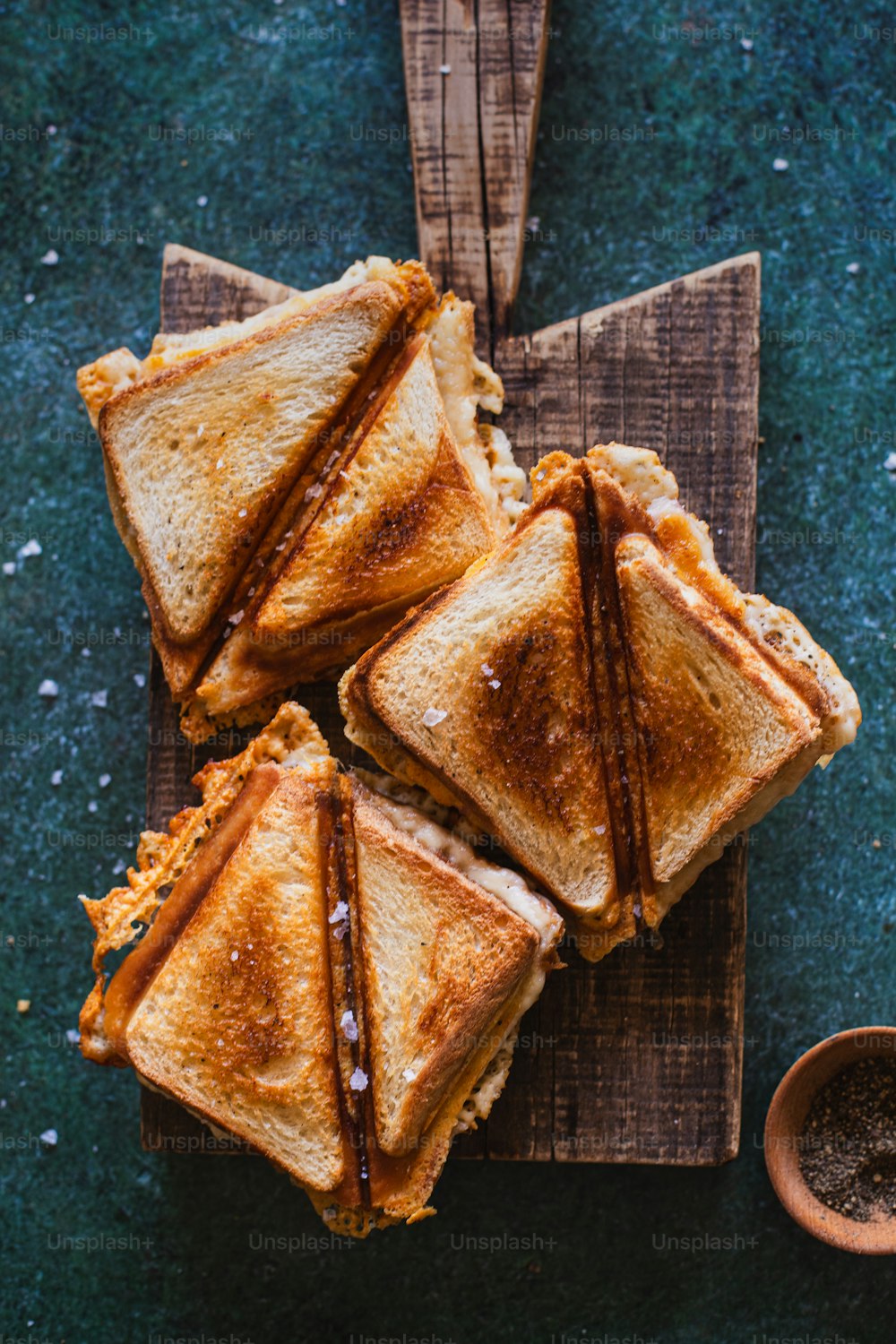 four grilled sandwiches on a cutting board with a wooden spoon