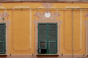 a yellow building with green shutters and a clock