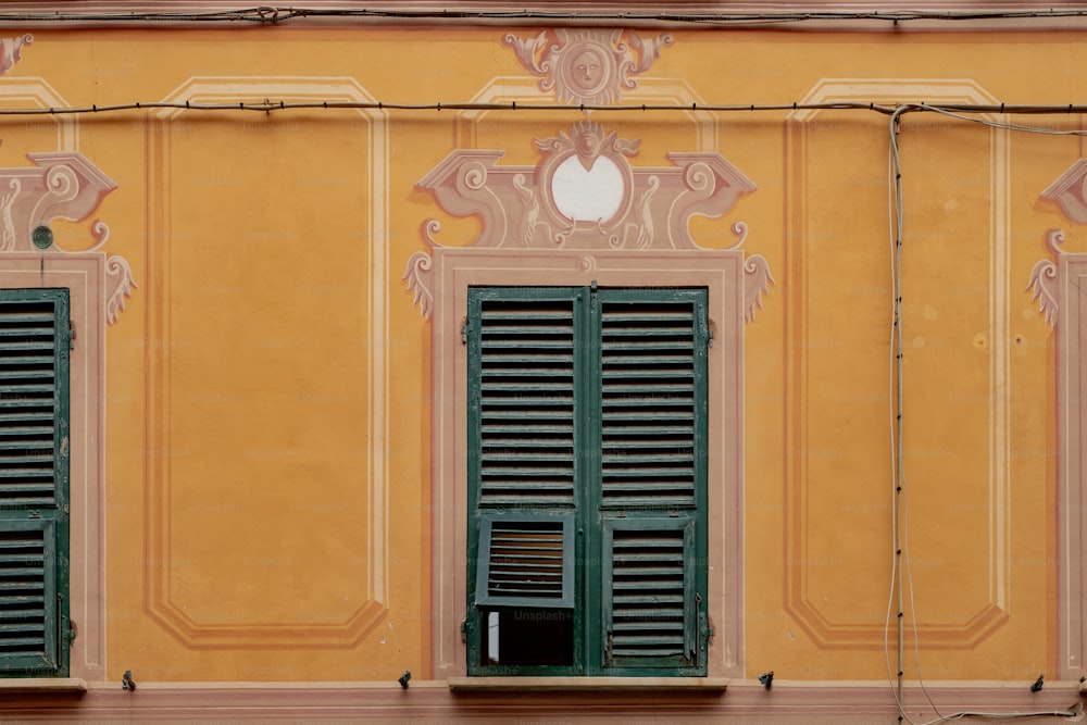 a yellow building with green shutters and a clock