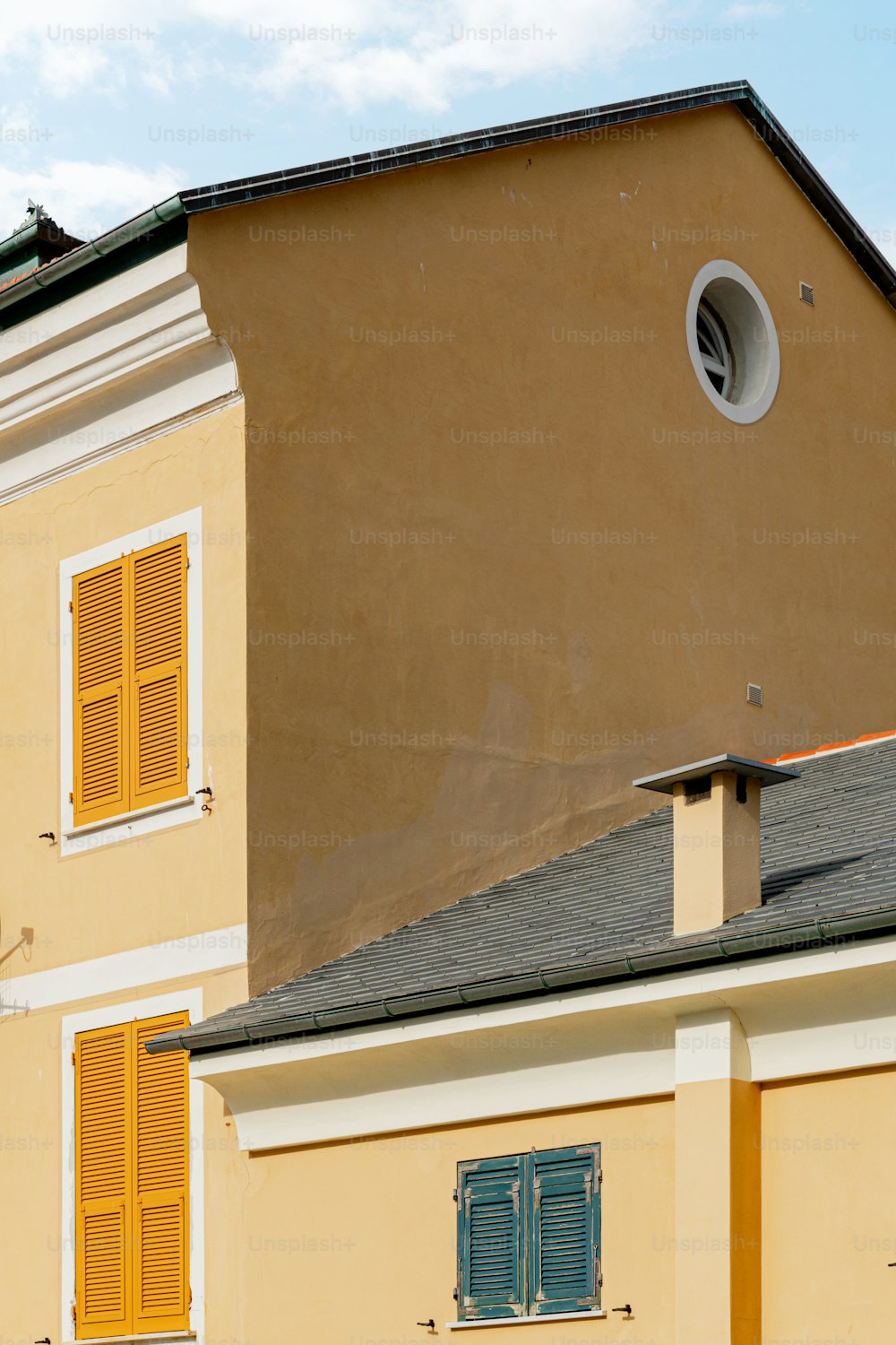 Ein hellbraunes Gebäude mit gelben Fensterläden und einer Uhr