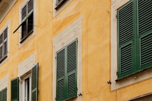 a yellow building with green shutters and a clock