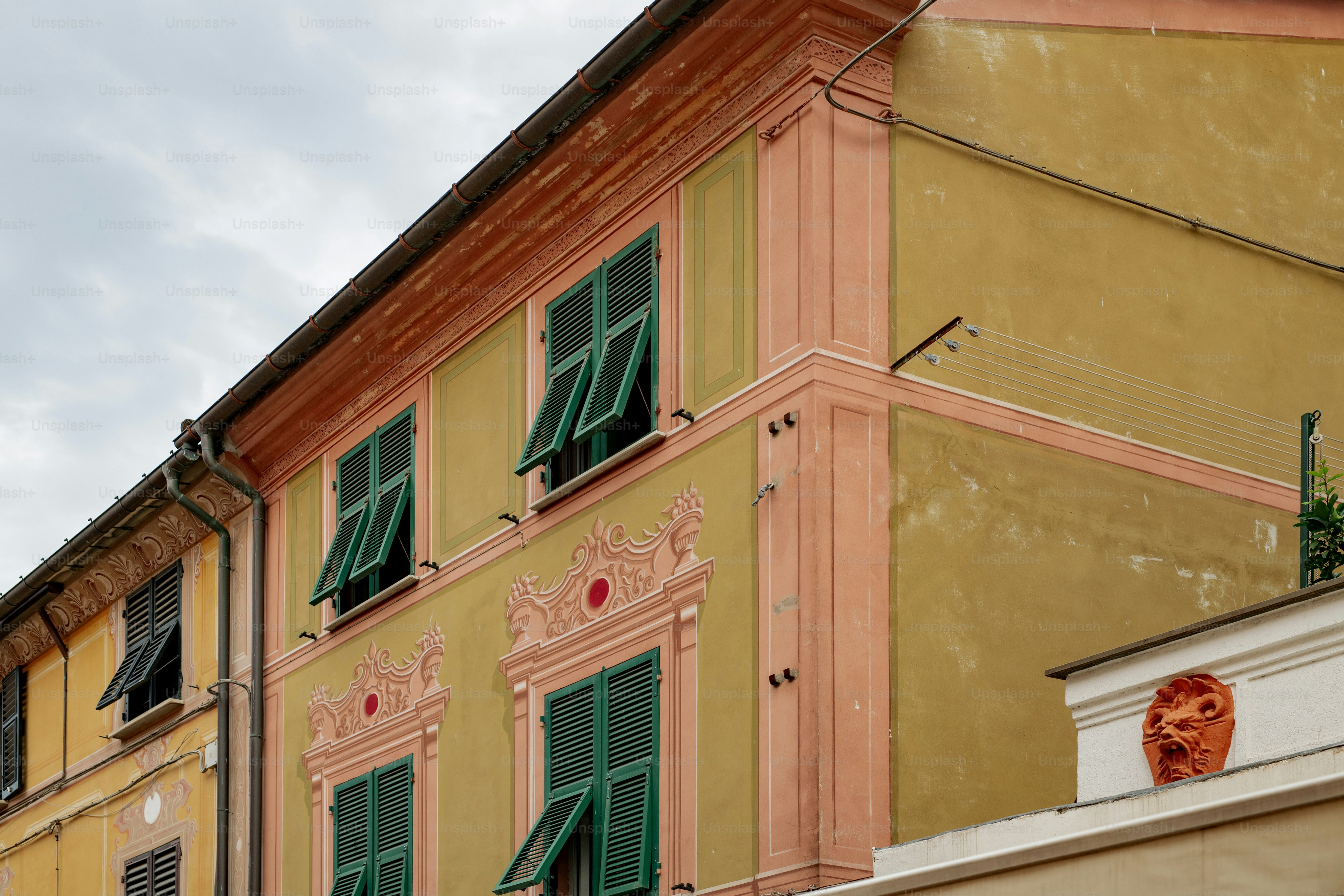 a yellow building with green shutters and a clock