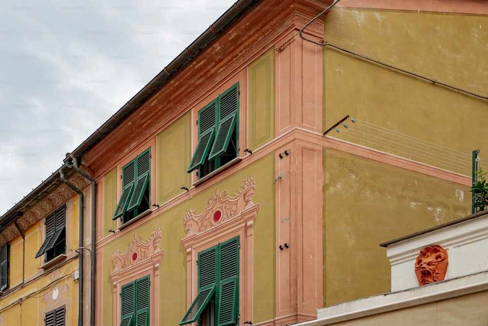 a yellow building with green shutters and a clock