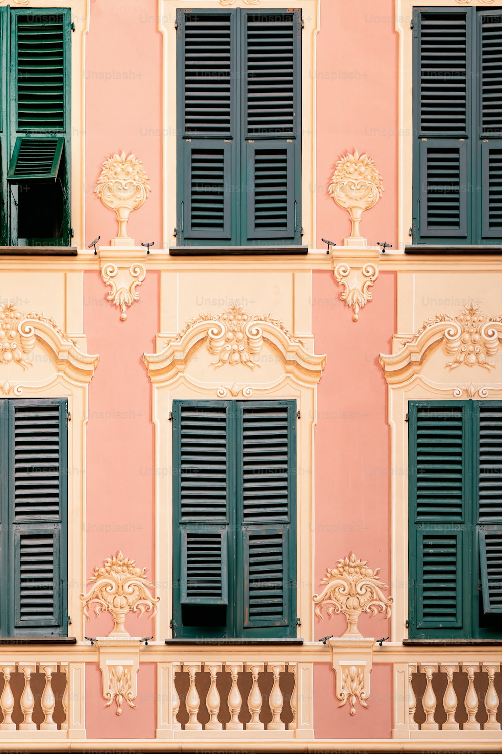 a pink building with green shutters and a clock