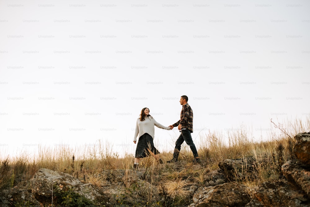 a man and a woman holding hands walking across a field