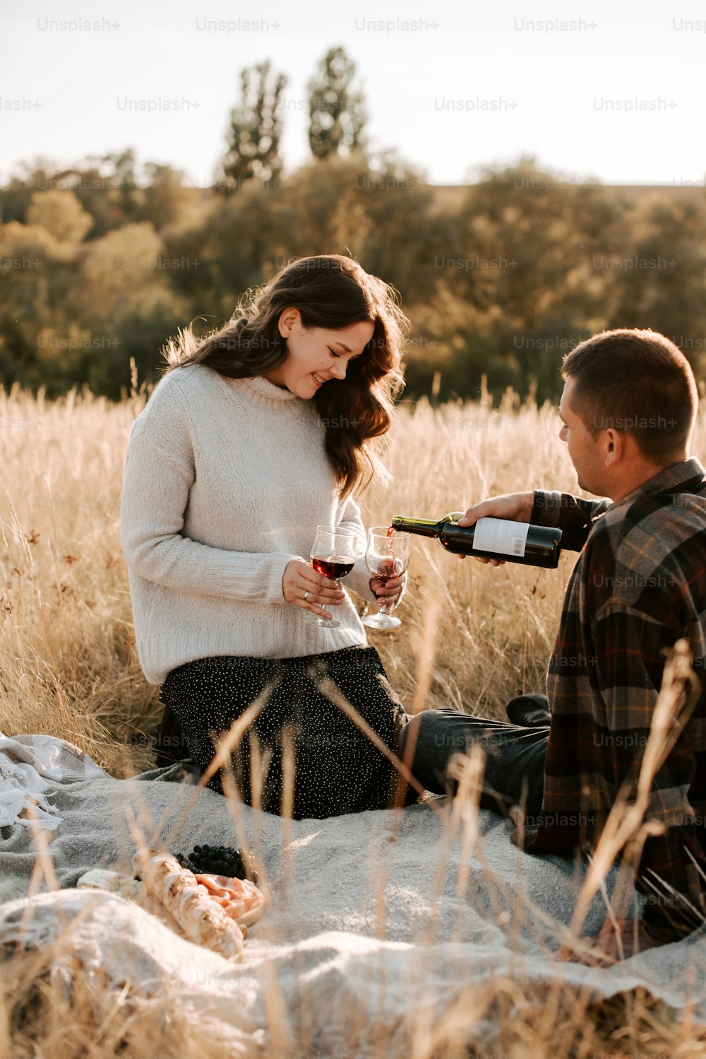 a man and a woman sitting in a field with a bottle of wine