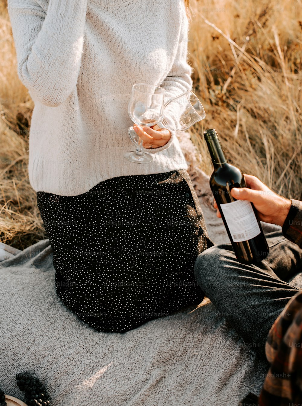 a woman holding a bottle of wine while sitting on a blanket