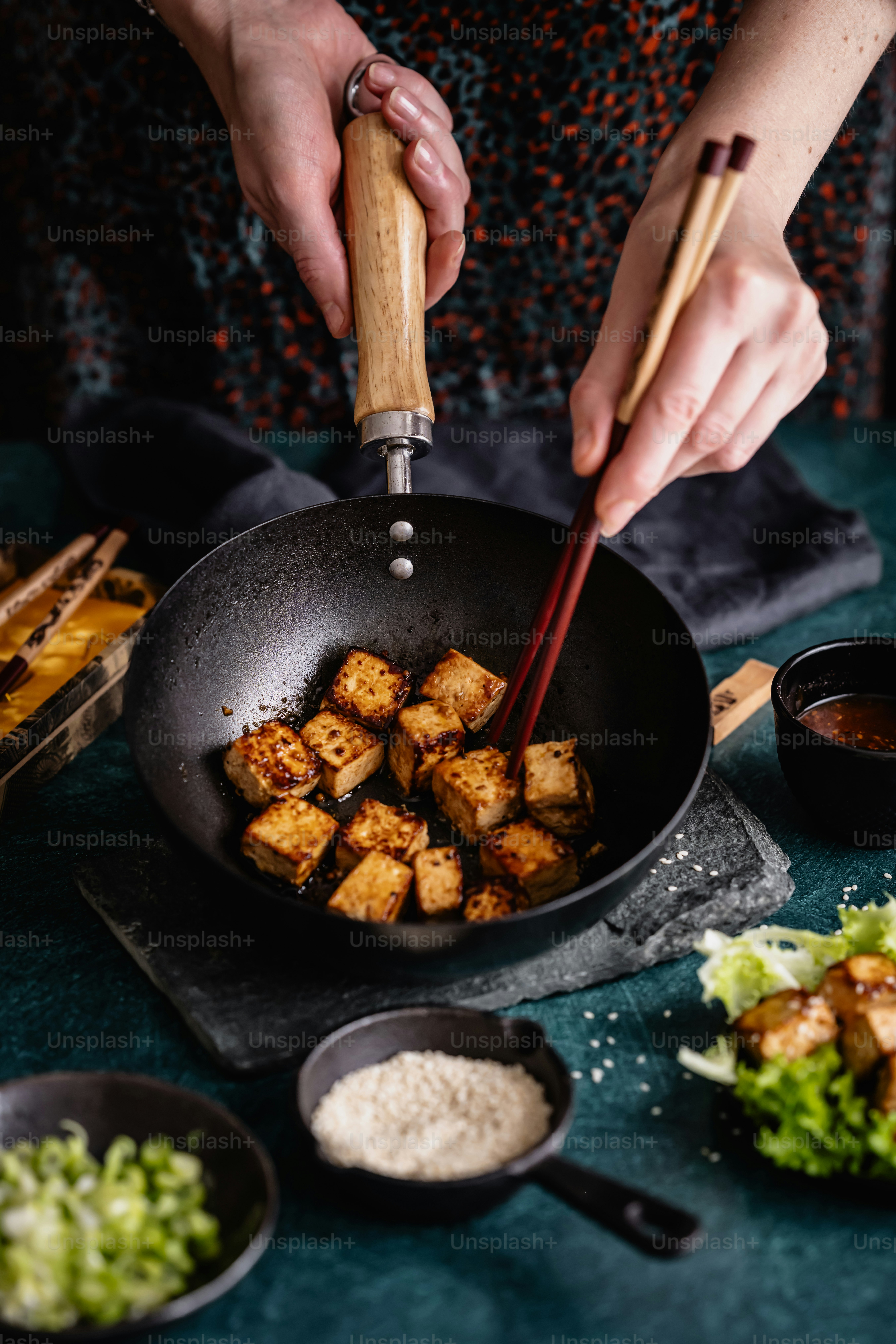 a woman stir frying tofu in a wok with chopsticks