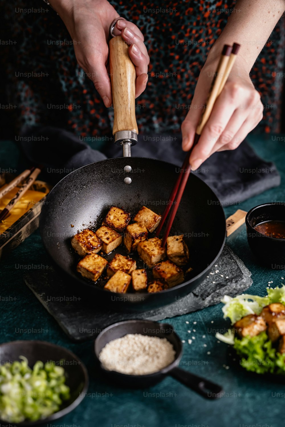 a woman stir frying tofu in a wok with chopsticks