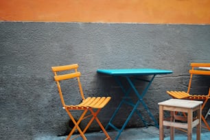 Deux chaises jaunes et une table bleue devant un mur gris
