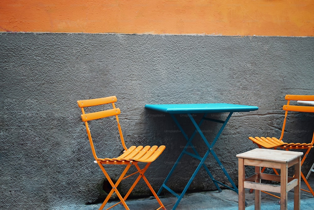 duas cadeiras amarelas e uma mesa azul em frente a uma parede cinza