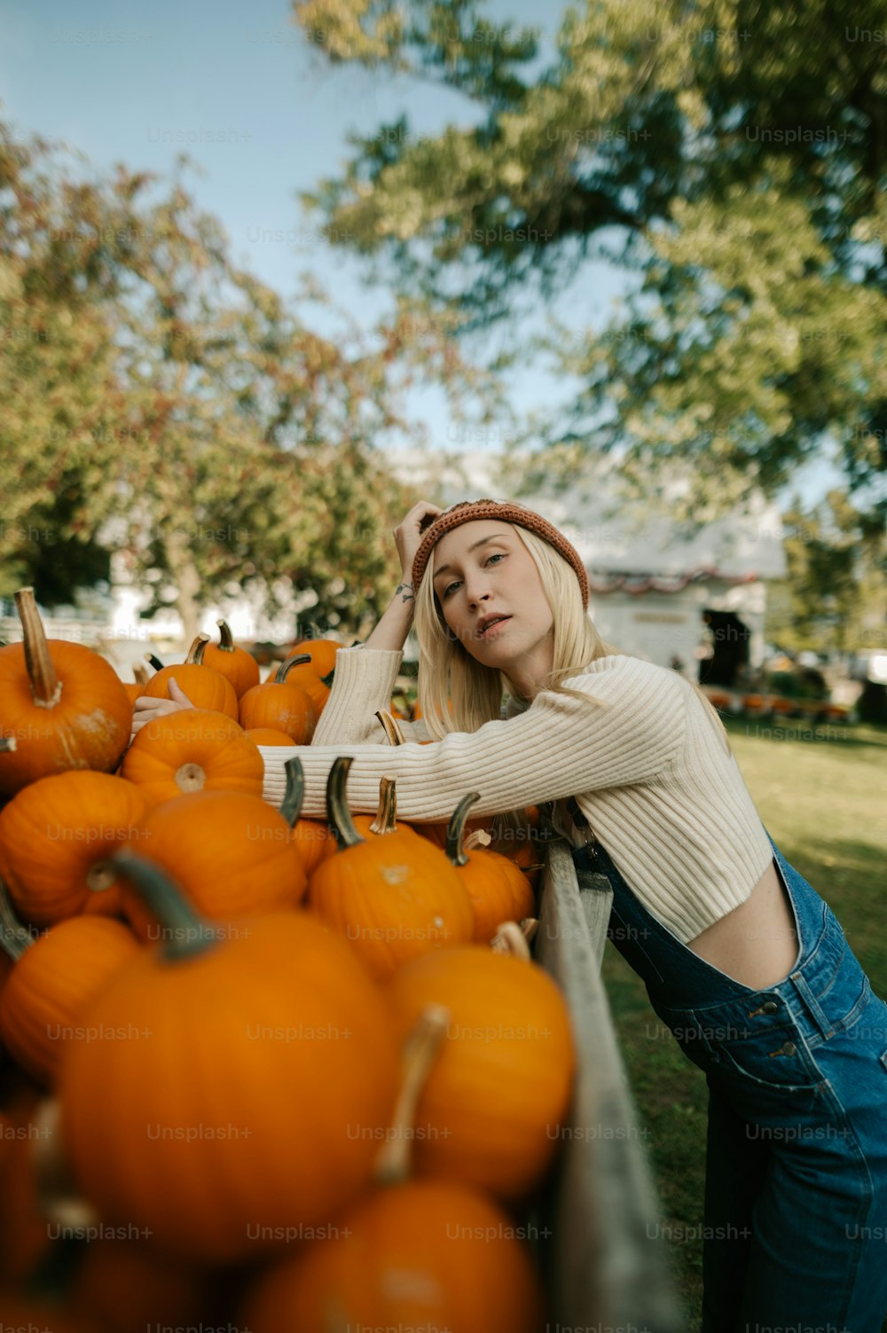 a woman leaning on a rail next to a pile of pumpkins
