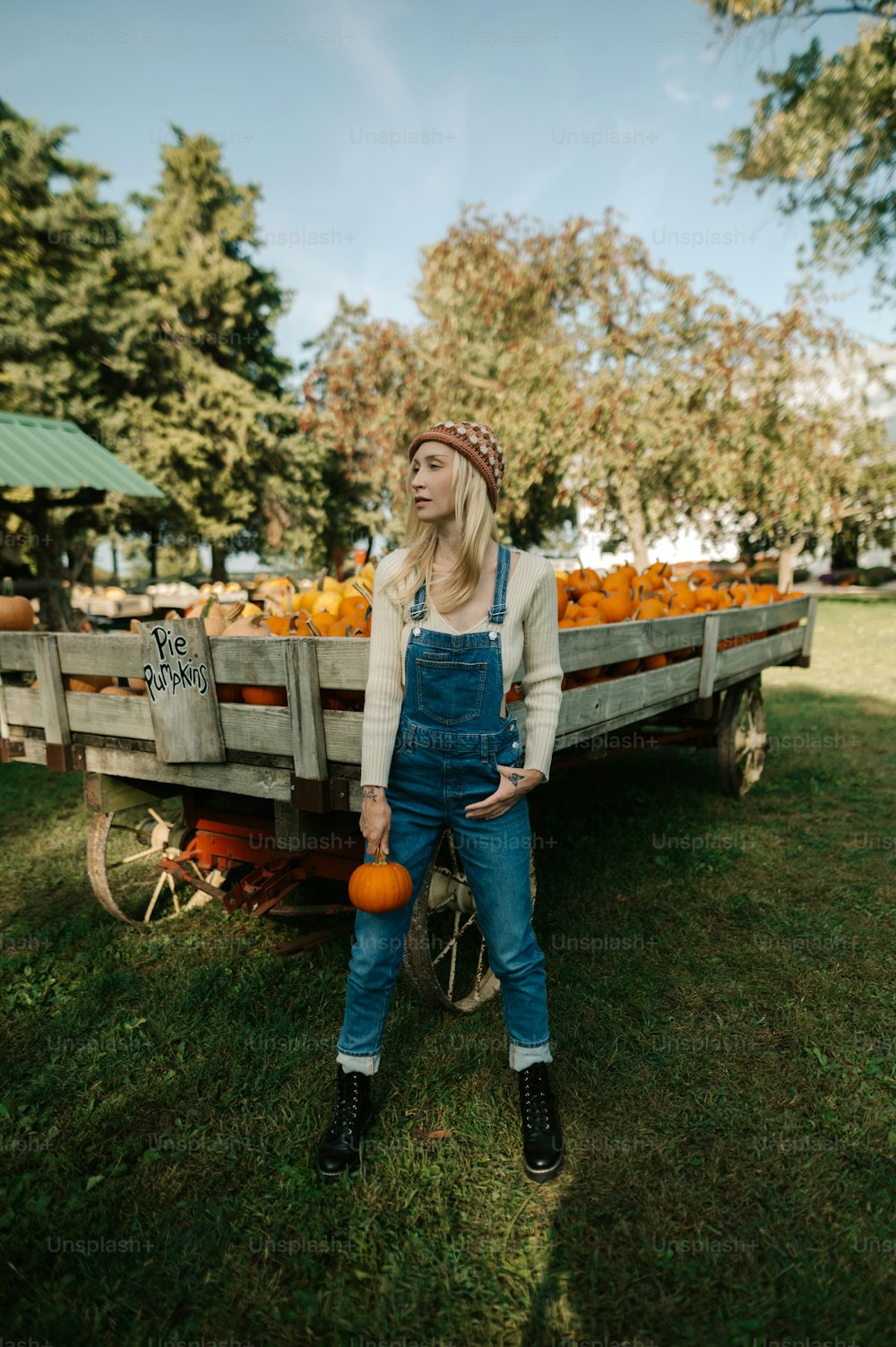 a woman standing next to a wagon full of pumpkins