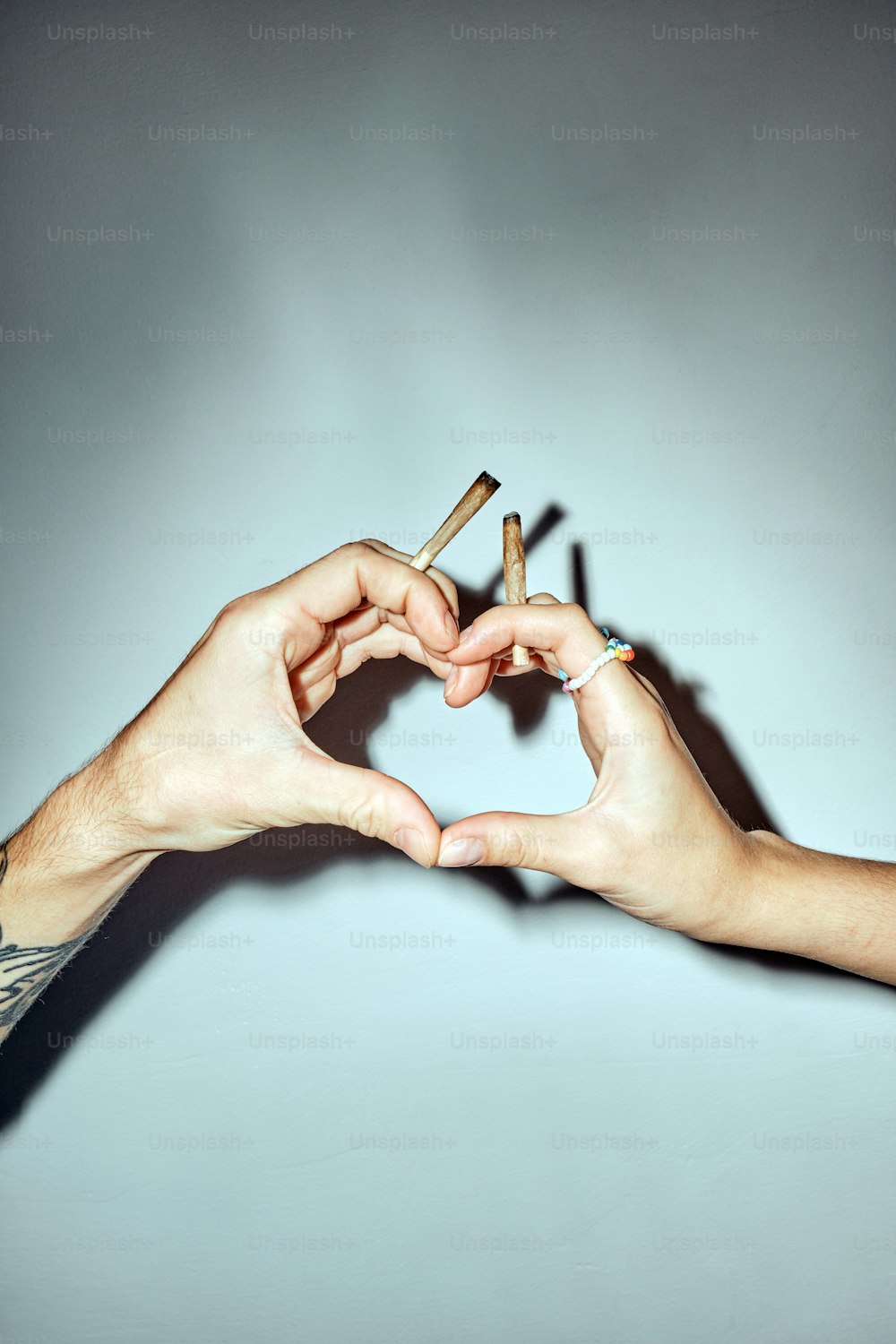 two hands making a heart shape with cigarettes
