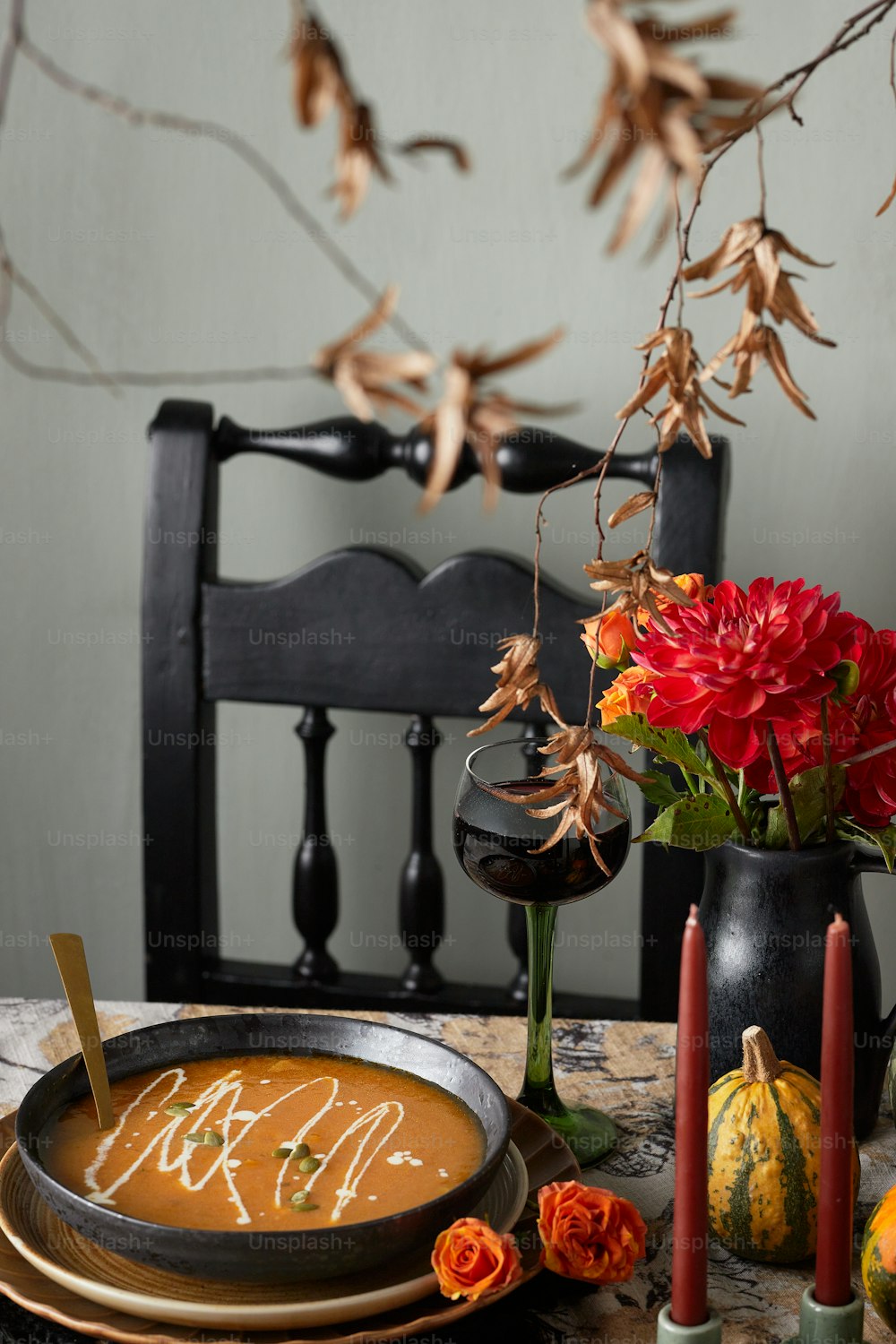 a table topped with a bowl of soup next to a vase of flowers