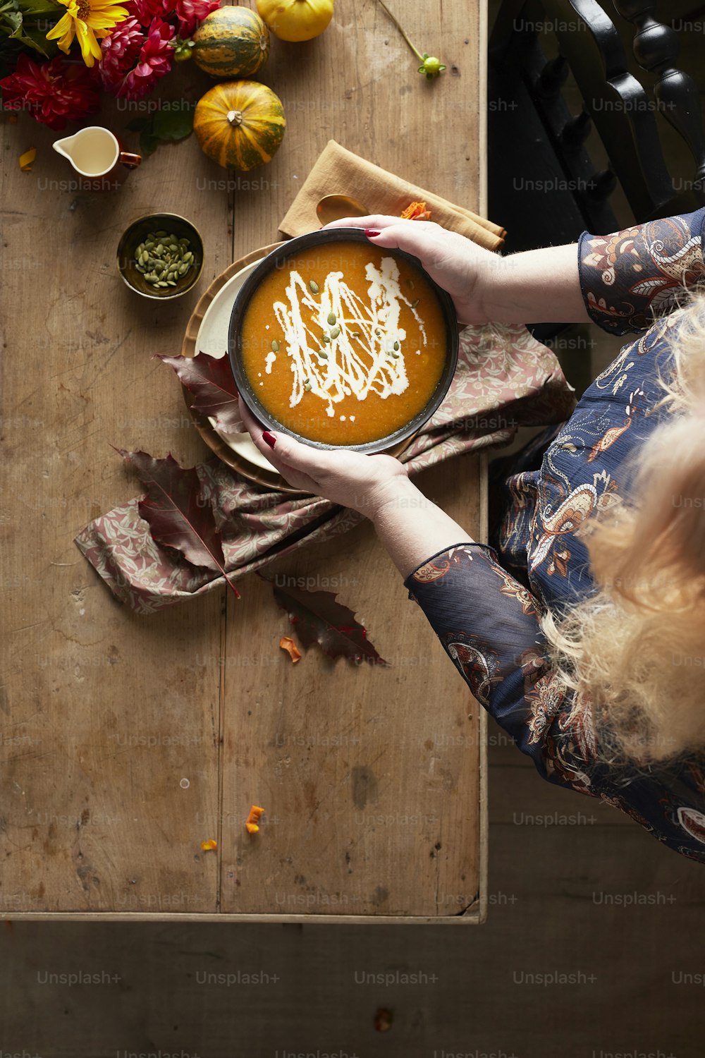 a woman holding a bowl of soup on top of a wooden table