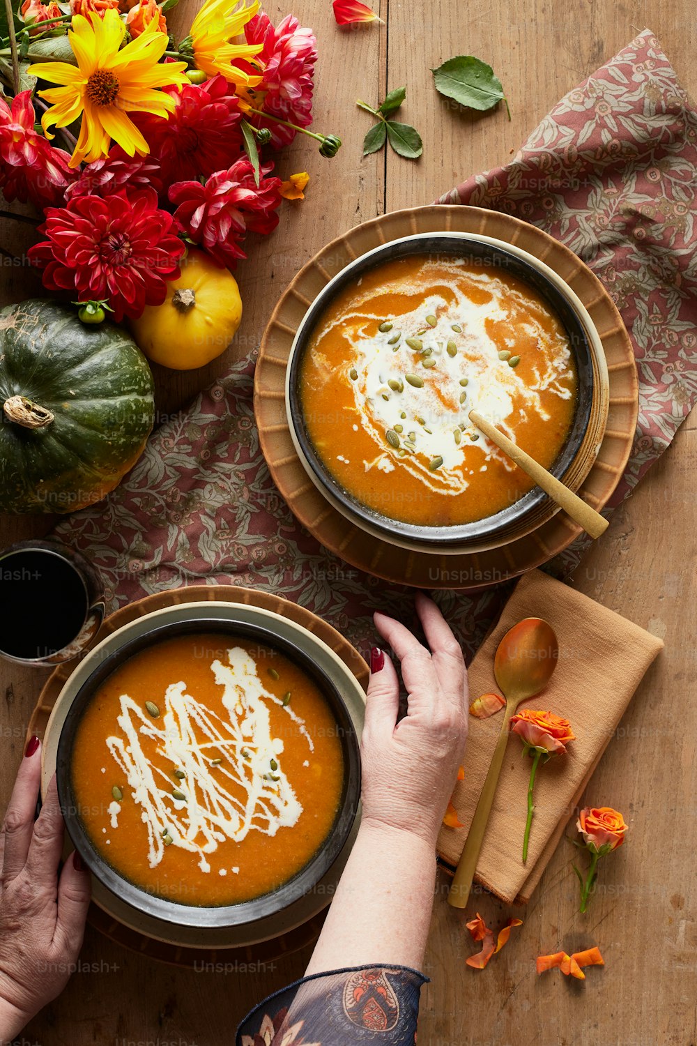 two bowls of carrot soup with a hand reaching for one