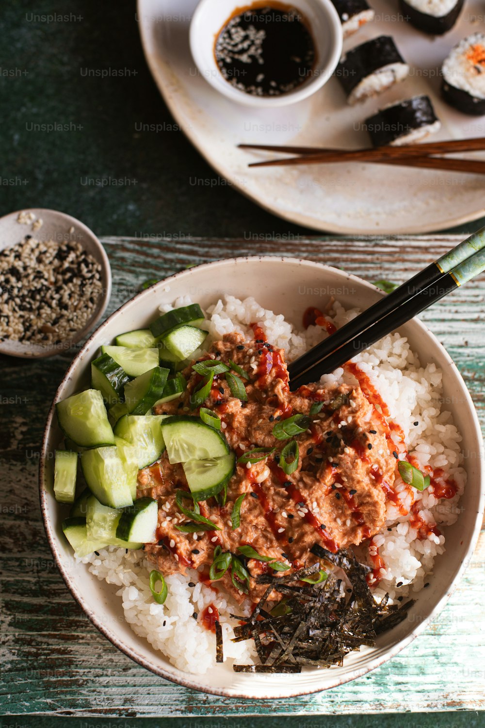 a bowl of rice, cucumbers, and sauce on a table