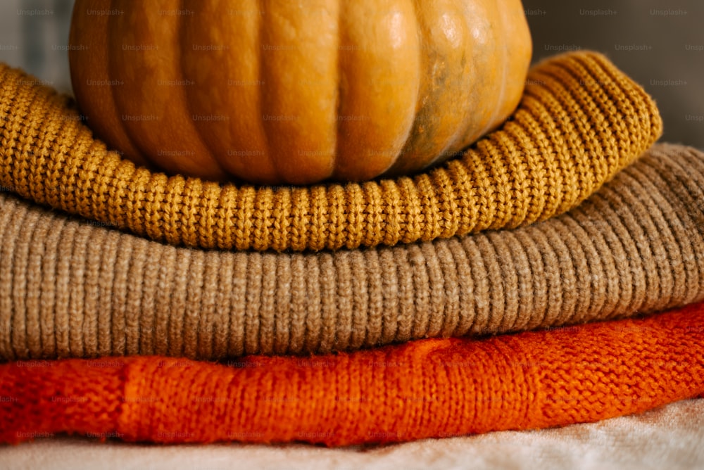 a pumpkin sitting on top of a pile of sweaters
