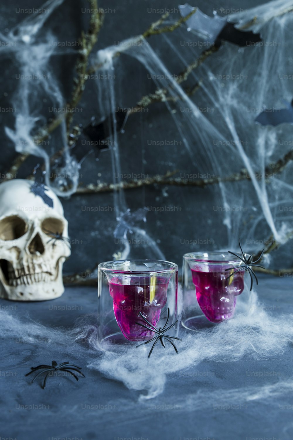 two glasses with pink liquid in front of a skull