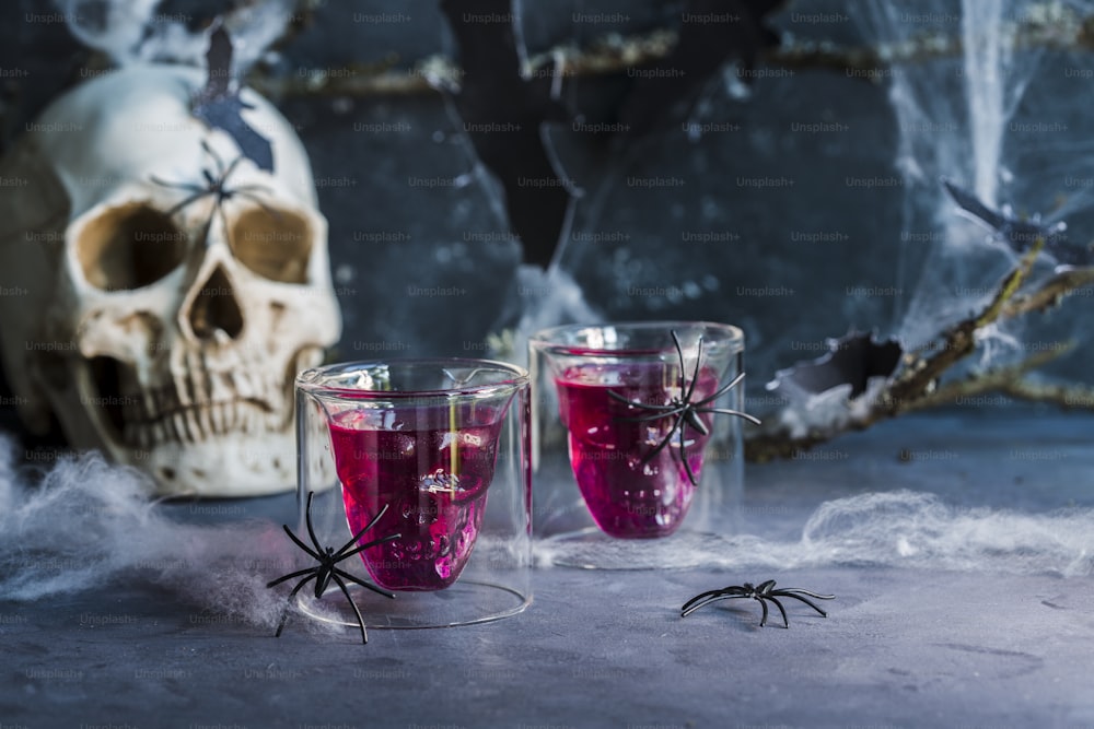 two glasses filled with liquid next to a skull