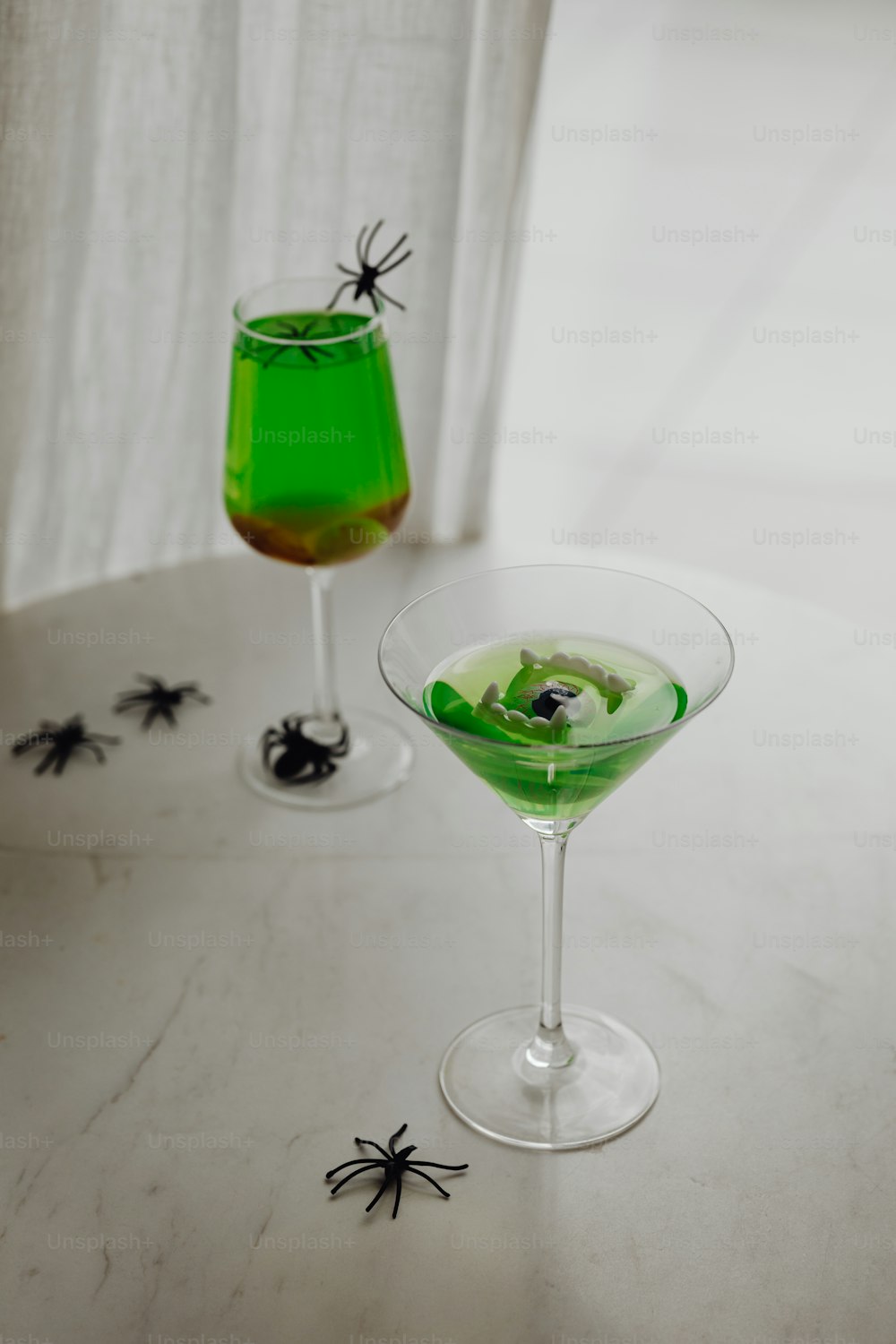 two glasses of green liquid with black spider decorations