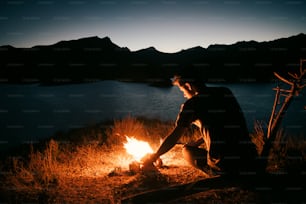 a man sitting in front of a campfire at night