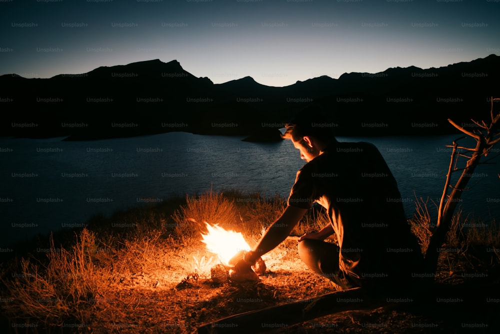 a man sitting in front of a campfire at night