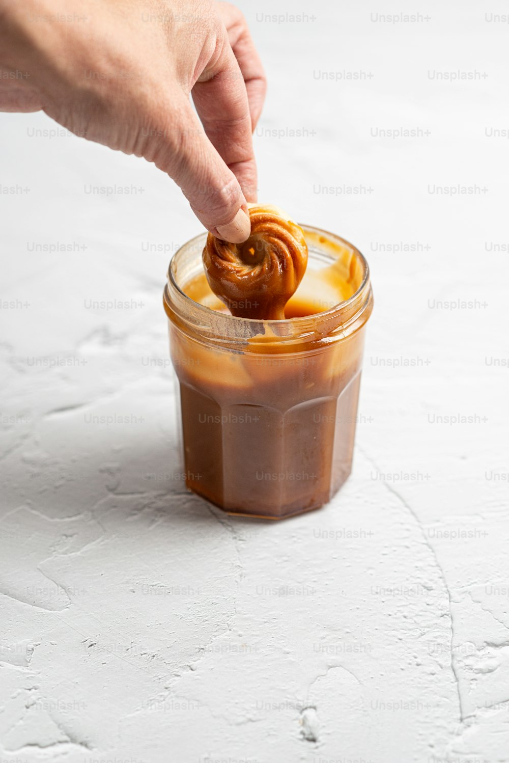 a person dipping a pretzel into a jar of caramel
