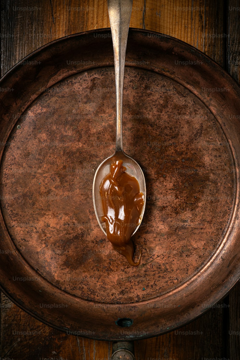 a spoon filled with caramel sauce on top of a wooden table