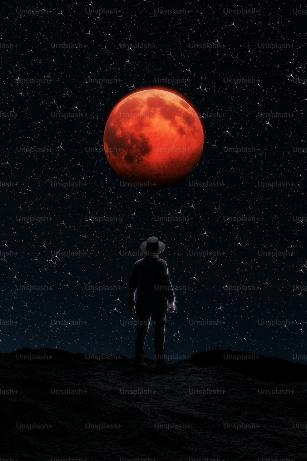 Un homme debout au sommet d’une colline sous une lune rouge