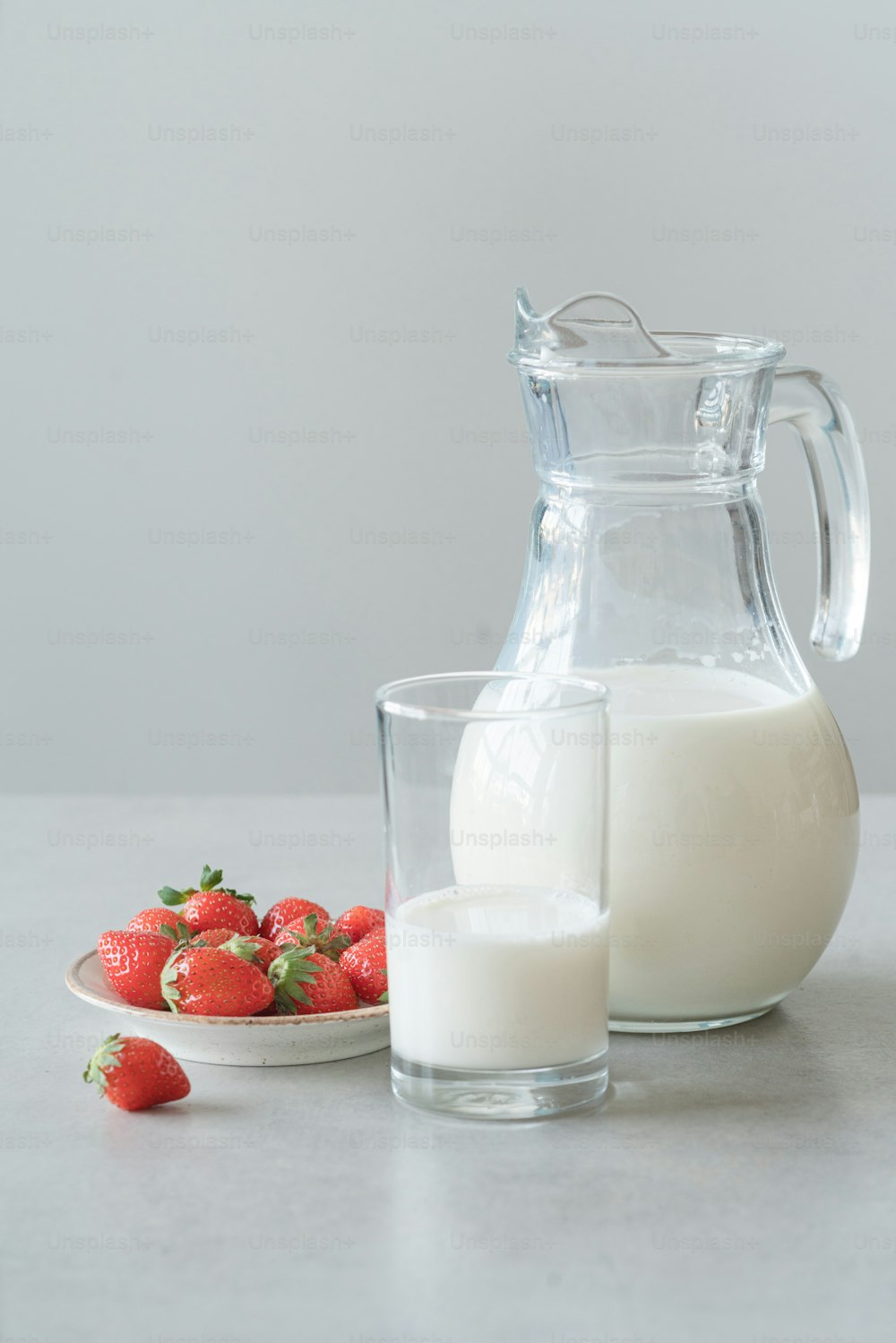 a pitcher of milk next to a plate of strawberries
