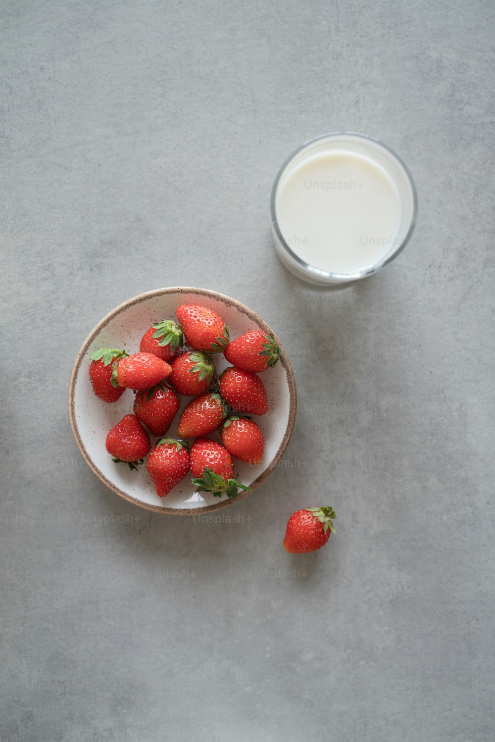 a bowl of strawberries next to a glass of milk