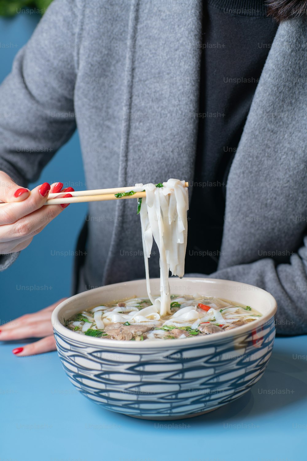 a woman eating a bowl of soup with chopsticks