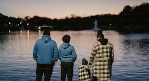 a group of three people standing next to a body of water