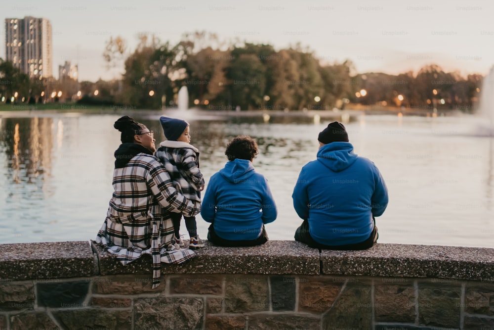 three people sitting on a wall looking at the water