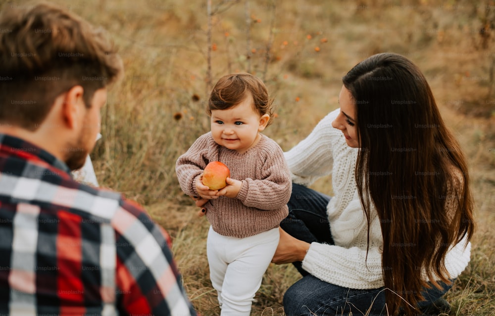un bebé sosteniendo una manzana mientras está de pie junto a dos adultos