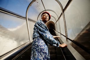 a woman in a blue dress and a red hat on an escalator