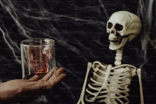 a person holding a glass with a skeleton behind it