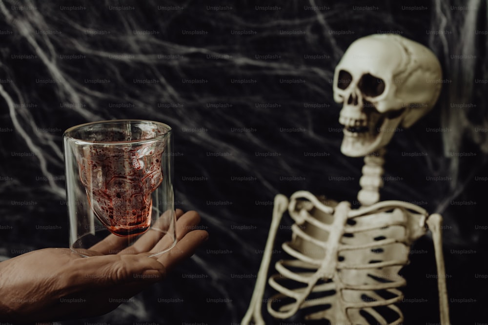 Una persona sosteniendo un vaso con un esqueleto detrás