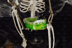 um esqueleto segurando uma bebida verde em um copo