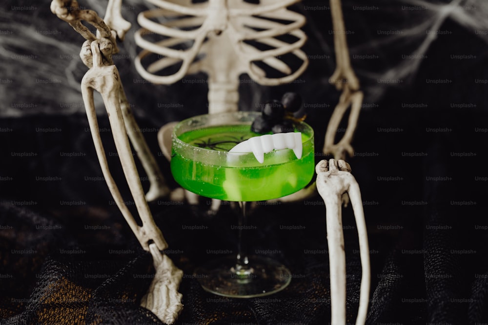 a skeleton holding a green drink in a glass