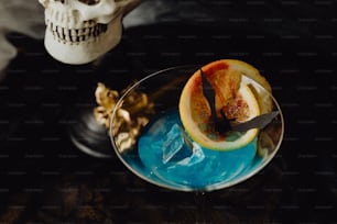 a blue cocktail with a slice of orange on the rim