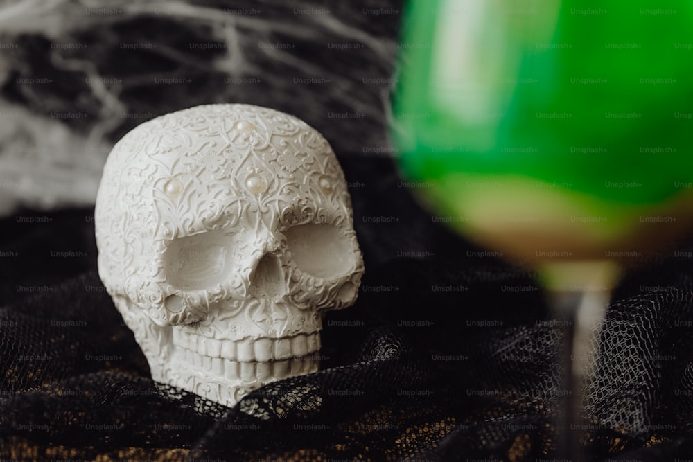 a white skull sitting next to a green glass