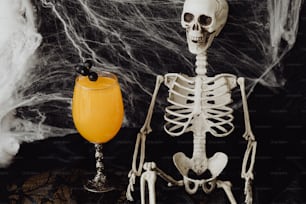 a skeleton sitting next to a glass of orange juice